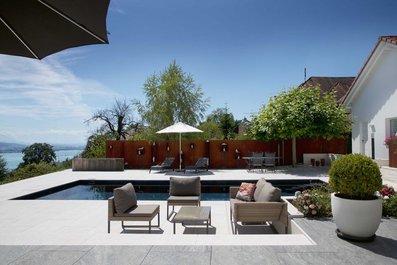 Von der Lounge aus wandert der Blick über den Pool und weiter zur Sichtschutzwand aus rohem Stahl, diee als Galerie für die Kunstobjekte dient. Die Terrasse schmiegt sich in verschiedenen Niveaus ans Haus.