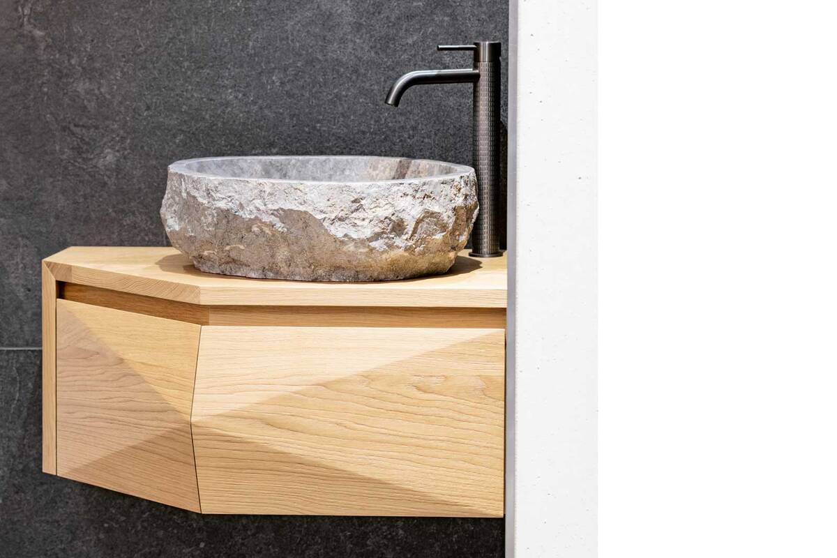 Die Eckbadmöbel aus massivem Eichenholz sind ideal für kleinere Badezimmer und bieten funktionale Eleganz. Sie werden ergänzt durch Flusssteinbecken, die aufgrund ihrer natürlichen Beschaffenheit jedes für sich ein Unikat darstellen. Schreinerei Fehlmann AG.
